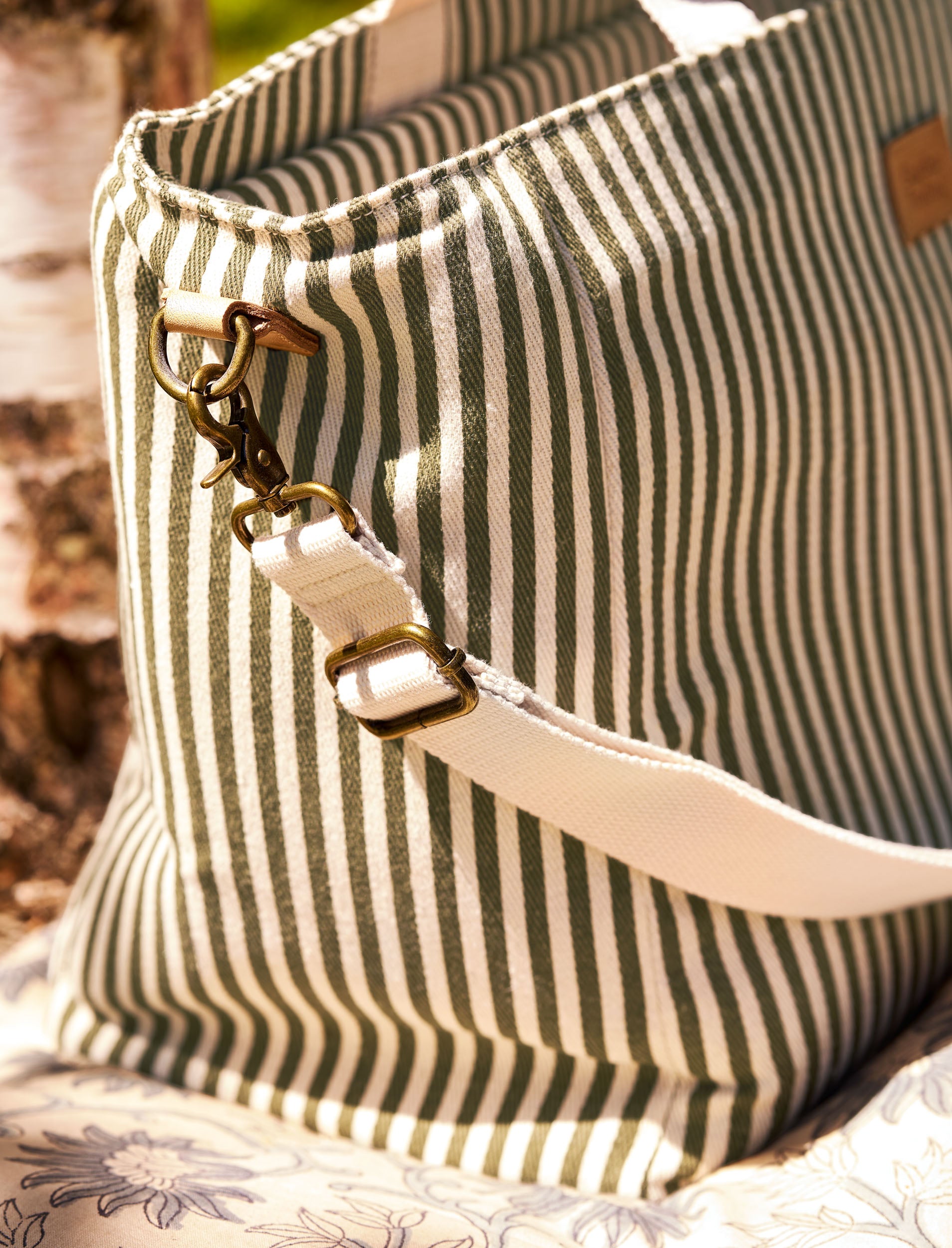 Striped picnic bag with a strap and decorative clasp on a textured surface
