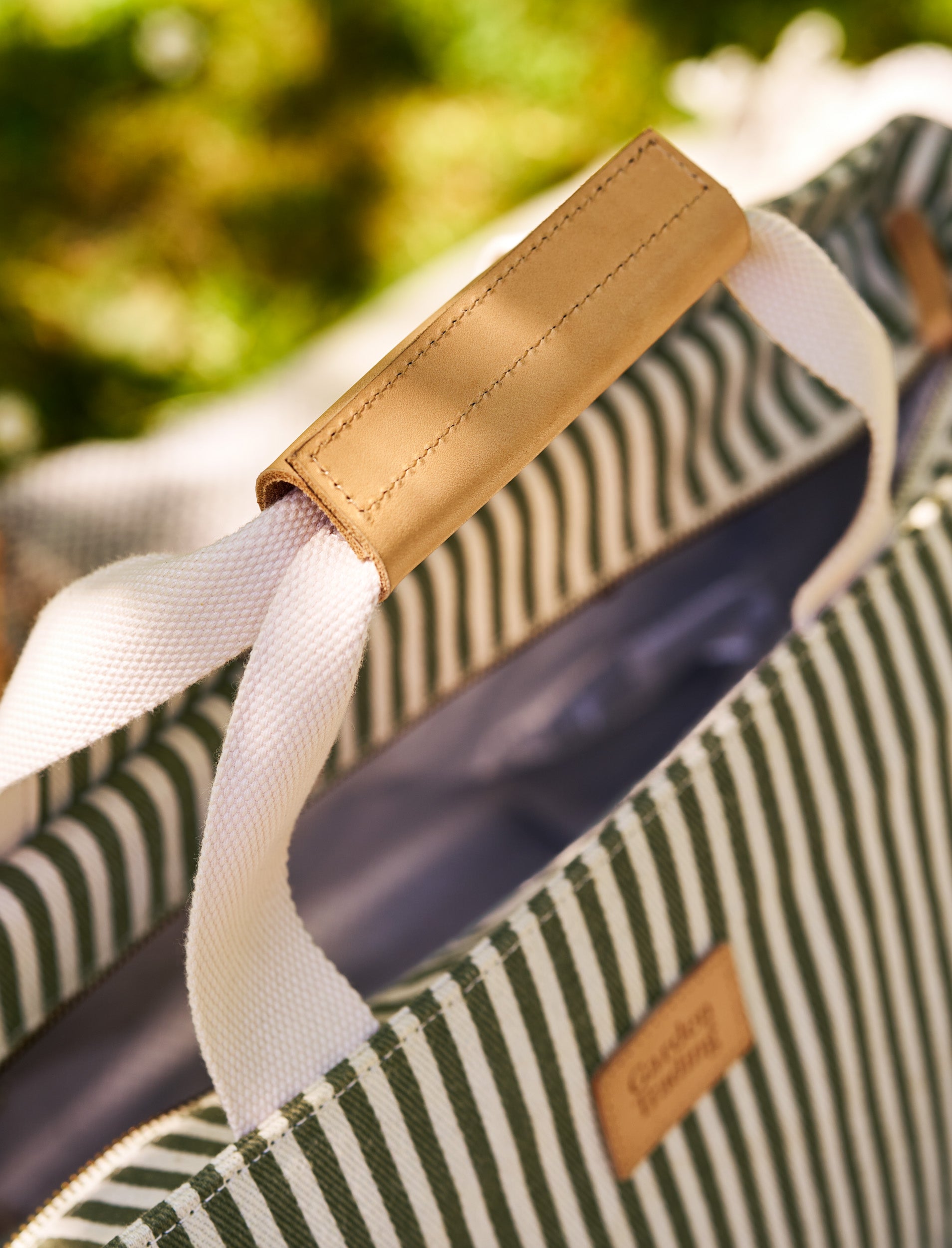 Close-up of a striped picnic bag with a leather handle and visible brand name.