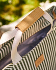 Close-up of a striped picnic bag with a leather handle and visible brand name.