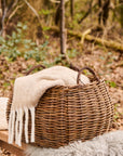 Woven square basket with a white blanket in a forest setting.