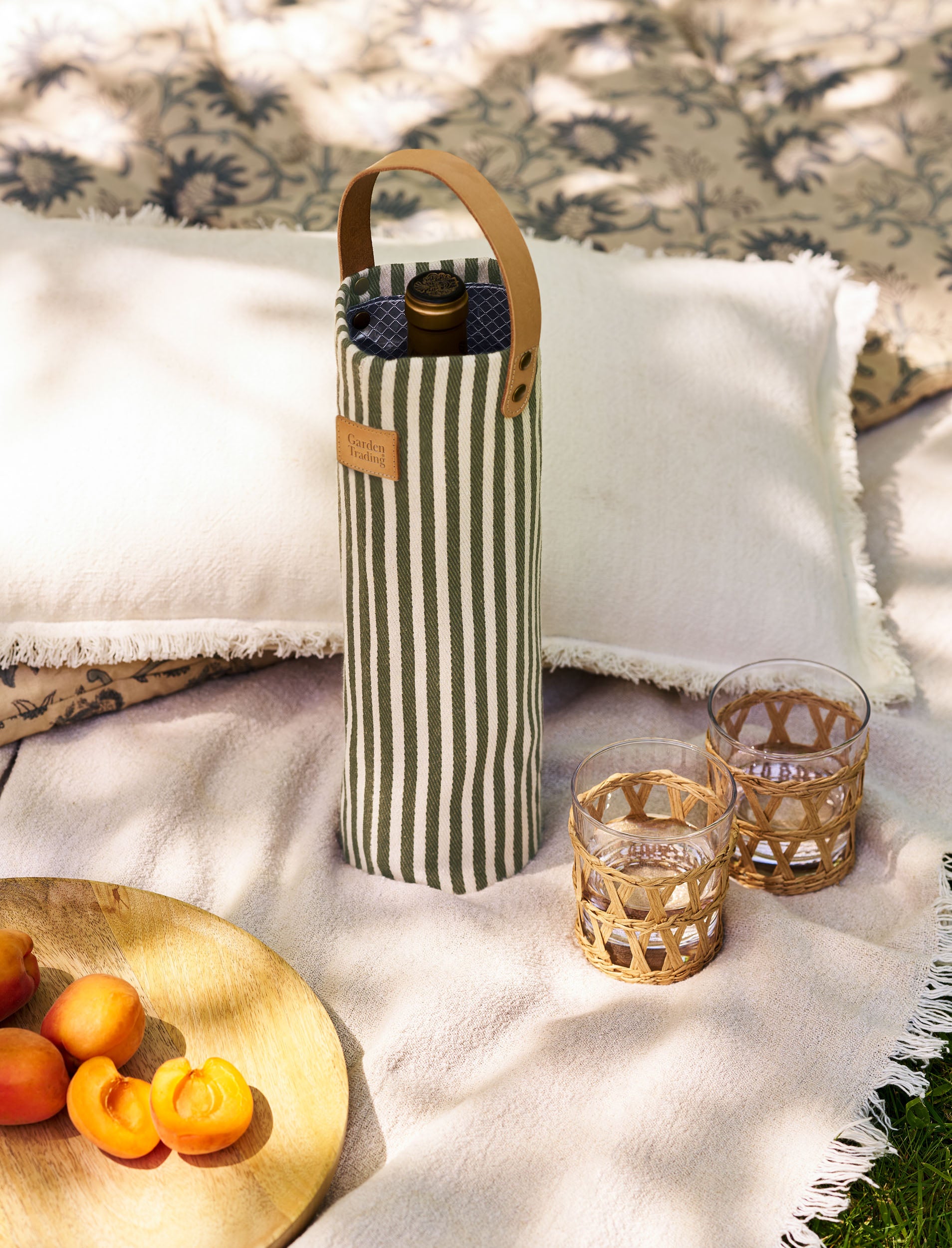 Wine bottle in a striped bottle bag with two glasses on a blanket outdoors