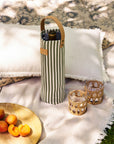 Wine bottle in a striped bottle bag with two glasses on a blanket outdoors