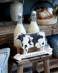 Farm fresh milk cow decor sign on a wooden bench with 2 jugs of milk.