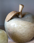 Ceramic apple decor with a leaf on a wooden surface.
