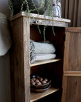 Close up of shelf on reclaimed wooden cabinet, filled with plants, textiles and ornaments.