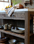 Wooden butchers block with marble top with rustic decor, including bowls and a loaf of bread.