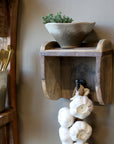 Wooden wall hook & shelf with a bowl, plant, and garlic hanging on a neutral wall.