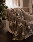 Neutral Christmas throw with Bambi reindeer print folded up on the arm of an armchair in front of Christmas Tree.