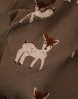 A close up of Neutral Christmas throw with Bambi reindeer print folded up on the arm of an armchair in front of fireplace.