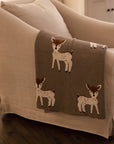 Neutral Christmas throw with Bambi reindeer print folded up on the arm of an armchair.
