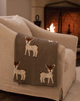 Neutral Christmas throw with Bambi reindeer print folded up on the arm of an armchair in front of fireplace.