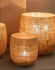 Set of three Jute Hurricane Lantern on stone fire place with lit candles inside.