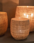 Set of three Jute Hurricane Lantern on stone fire place with lit candles inside.