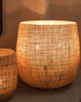 Jute Hurricane Lantern on stone fire place with lit candles inside.