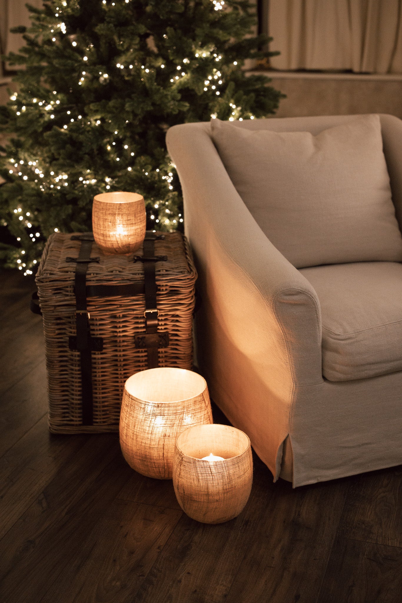 Set of three Jute Hurricane Lantern on side table in front of Christmas Tree.