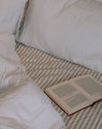 unmade white and striped bedding with an open book.
