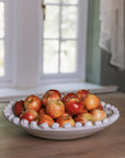 A white ceramic bobble bowl filled with red apples.