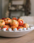 A white ceramic bobble bowl filled with red apples.