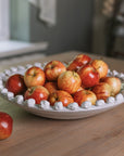A white ceramic bobble bowl filled with red apples.