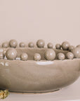 Grey ceramic bobble bowl with a lit candle and dried hops.