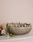 Grey ceramic bobble bowl with a lit candle and dried hops.