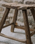 A reclaimed style wooden stool against a stone wall.
