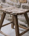 A reclaimed style wooden stool against a stone wall.
