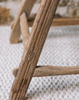 The leg of a reclaimed style wooden stool against a stone wall.