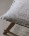 Pinstripe black and white linen cushion with frayed edge on wooden stool.