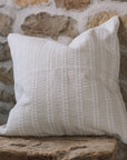 Cream and white stitch striped cushion on wooden stool against a stone wall.