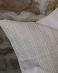 Cream and white stitch striped cushion on wooden stool against a stone wall.