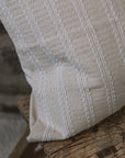 Cream and white stitch striped cushion on wooden stool against a stone wall.