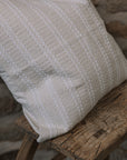 Cream and white stitch striped cushion on wooden stool against a stone wall.