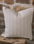 Cream and white stitch striped cushion on wooden stool against a stone wall.