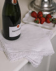 White linen napkin folded over with bobbles on the trim with champagne and strawberries.