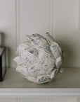 Distressed Artichoke Ornament on a white shelf.