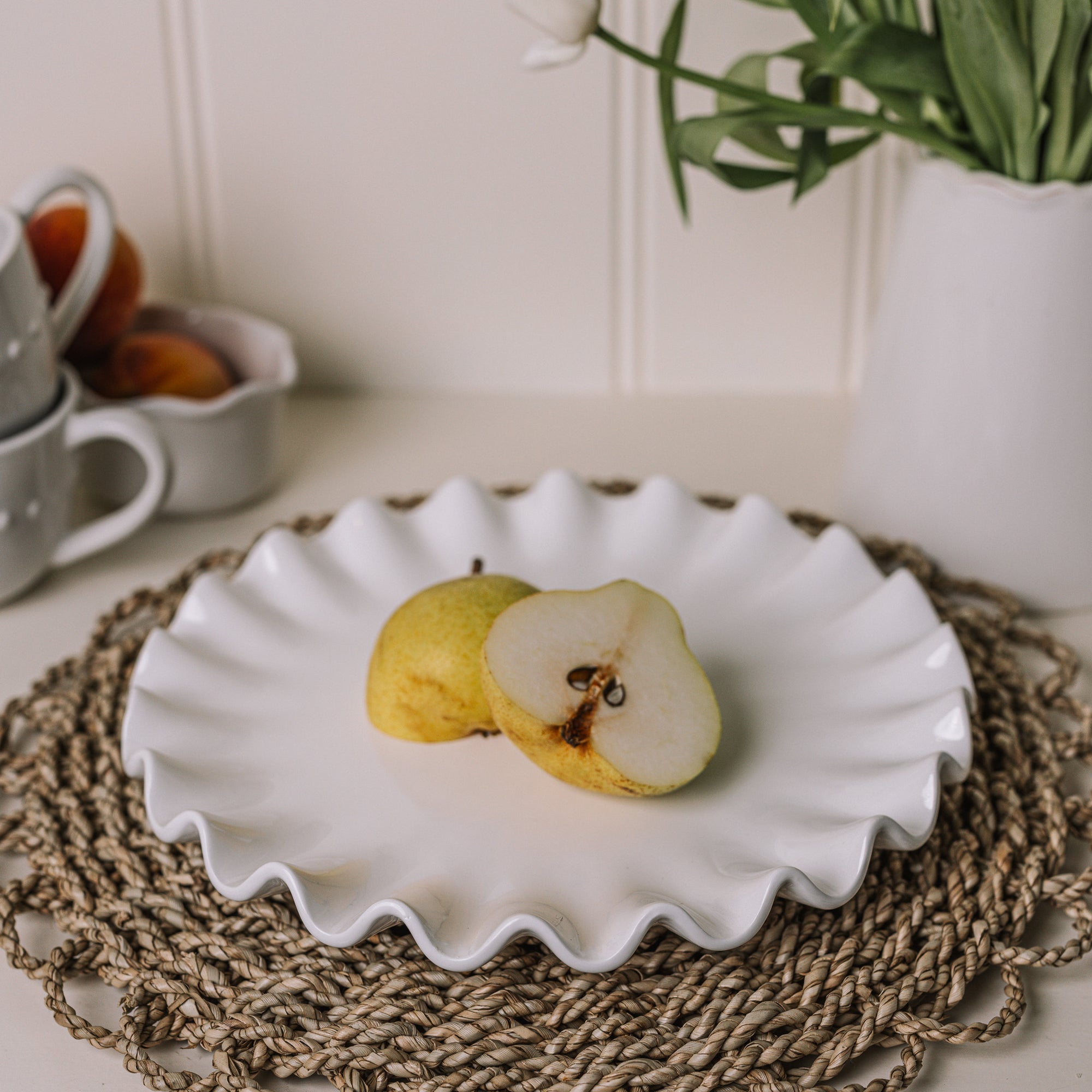 White ceramic cake plate with ruffled edges with a sliced pear on a rattan placemat.
