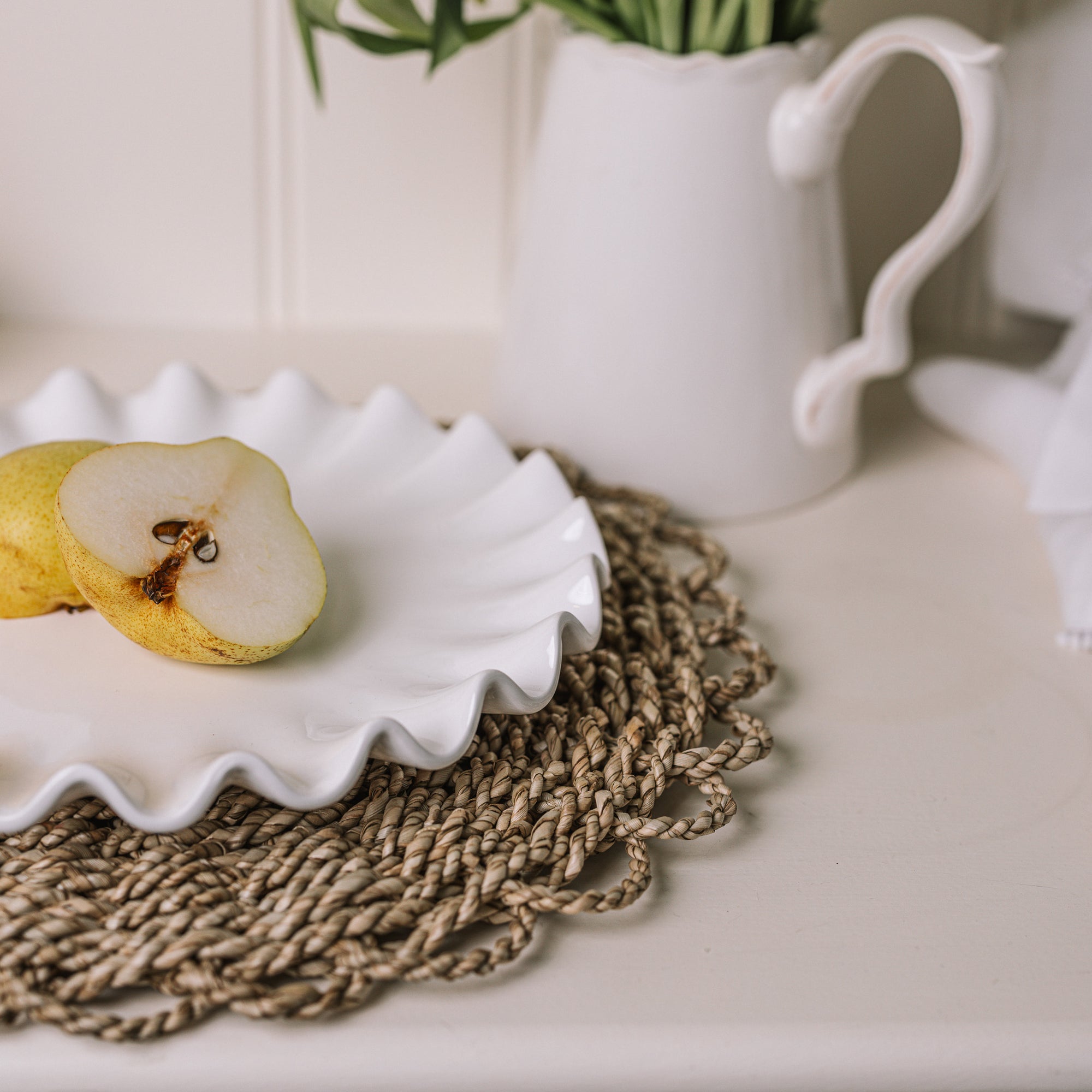 White ceramic cake plate with ruffled edges with a sliced pear on a rattan placemat.