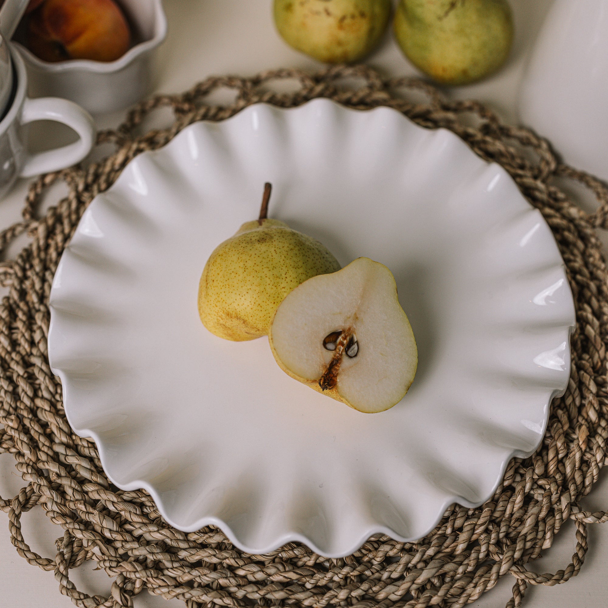 White ceramic cake plate with ruffled edges with a sliced pear on a rattan placemat.