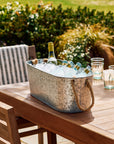 Metal ice drinks bucket with bottles of wine and water on a wooden table outdoors.