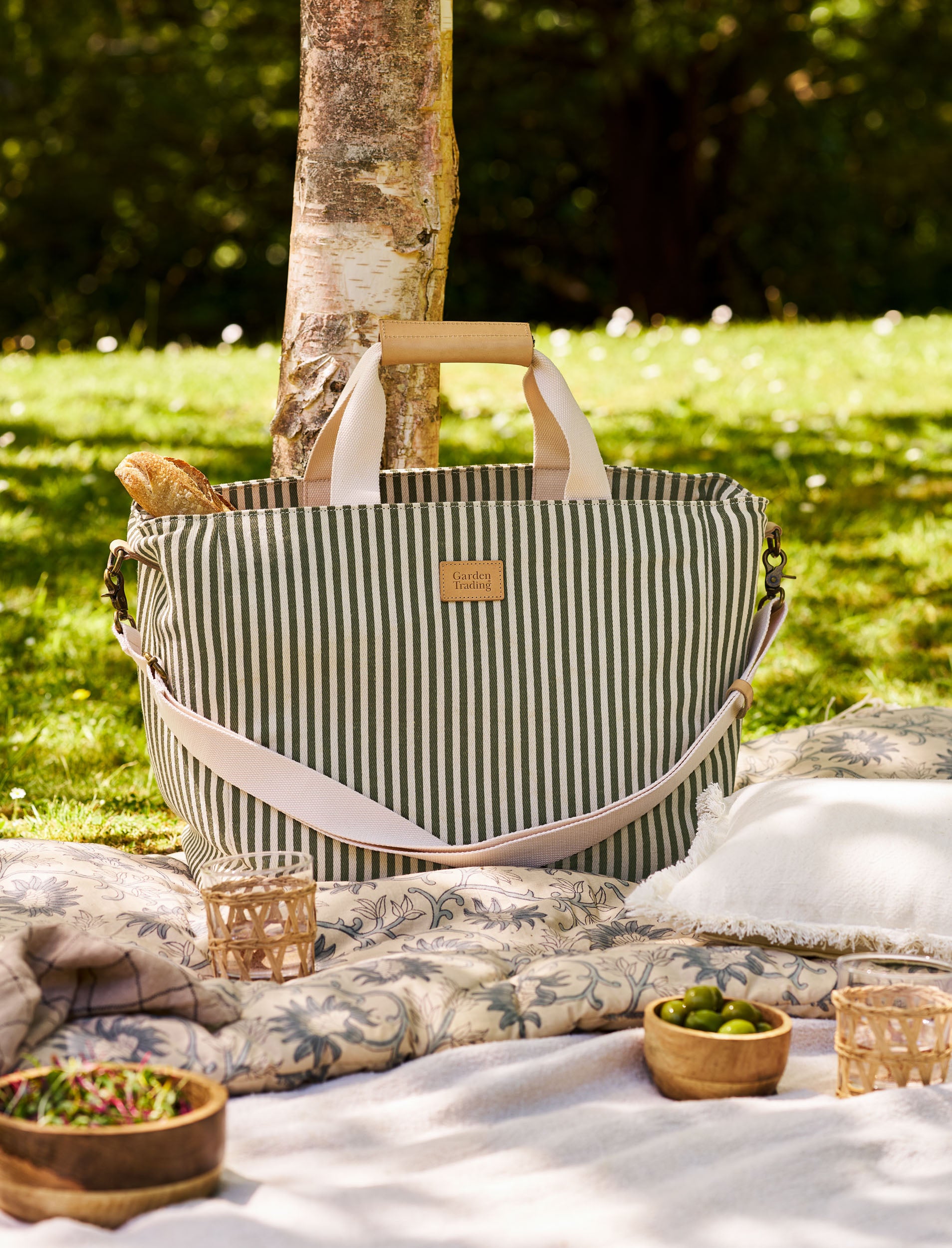 Striped picnic bag on a blanket with food and a tree in the background