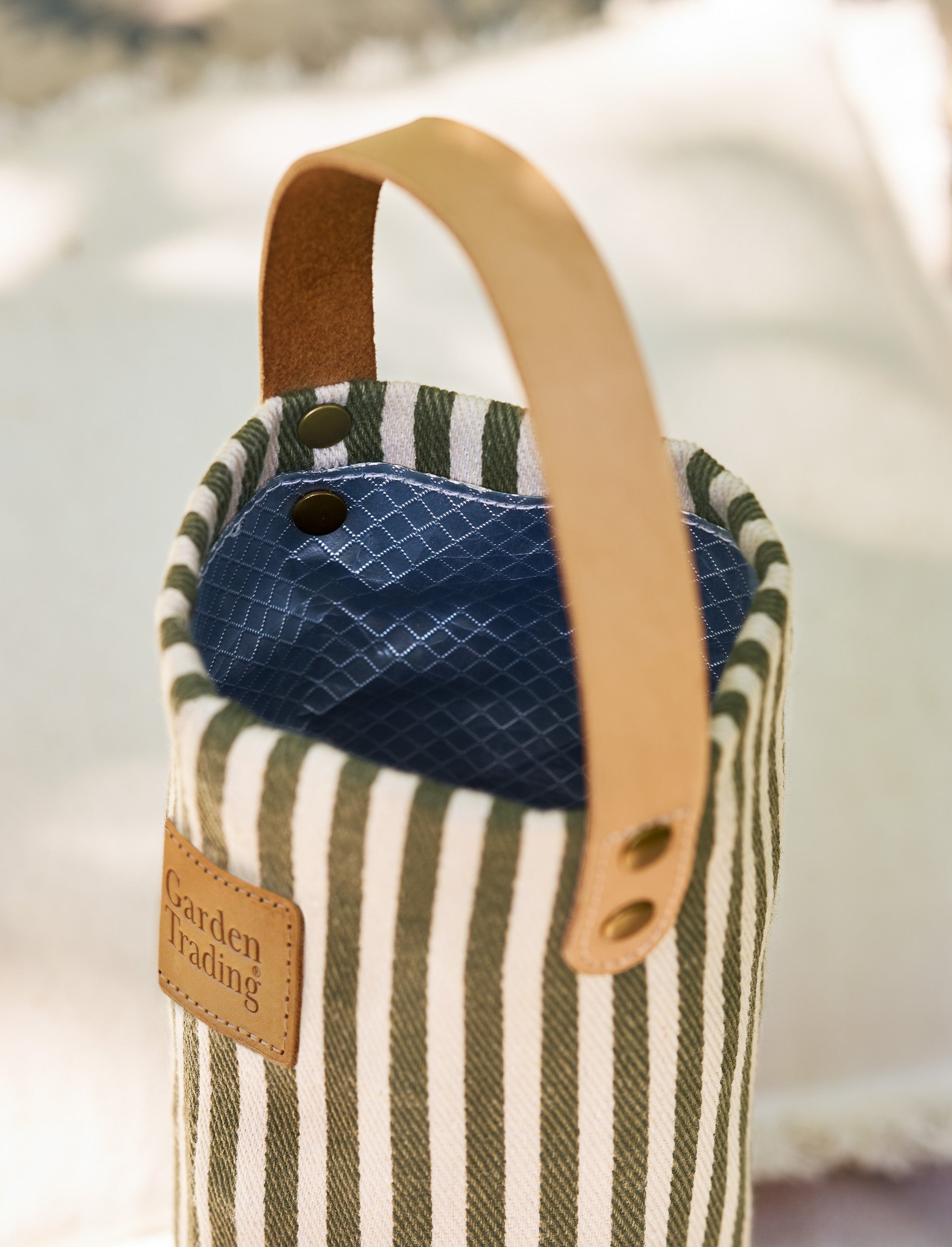 Striped fabric bottle bag with a blue interior and brown handle on a blurred background