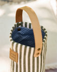 Striped fabric bottle bag with a blue interior and brown handle on a blurred background