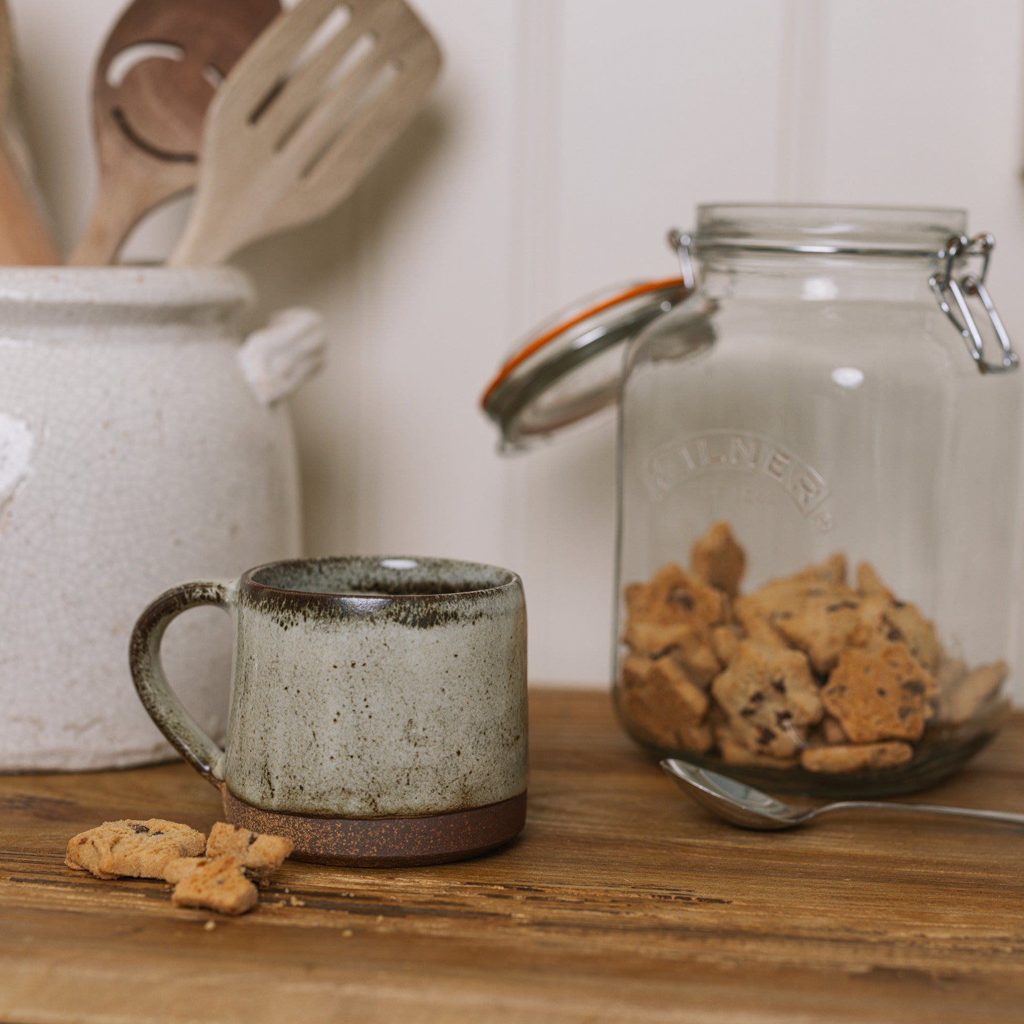 A brown speckled stoneware mug on wooden board with crumbled biscuit.