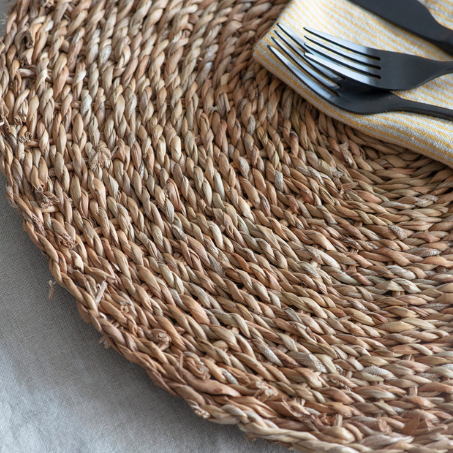 Close up of circular woven placemat with cutlery and napkin on top.