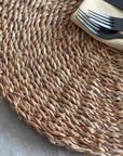 Close up of circular woven placemat with cutlery and napkin on top.