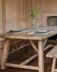 Large pine dining table in living room with dining benches and table settings for two.
