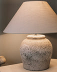 Antique grey lamp base with white lamp shade against a blue and black background.