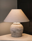 Antique grey lamp base with white lamp shade against a blue and black background.