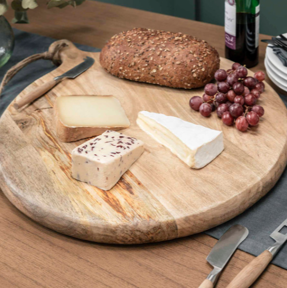 Round wooden serving board with jute rope loop, with cheese, bread and grapes on.